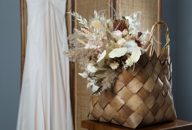 Stylish straw bag with beautiful dried flowers on chair indoors