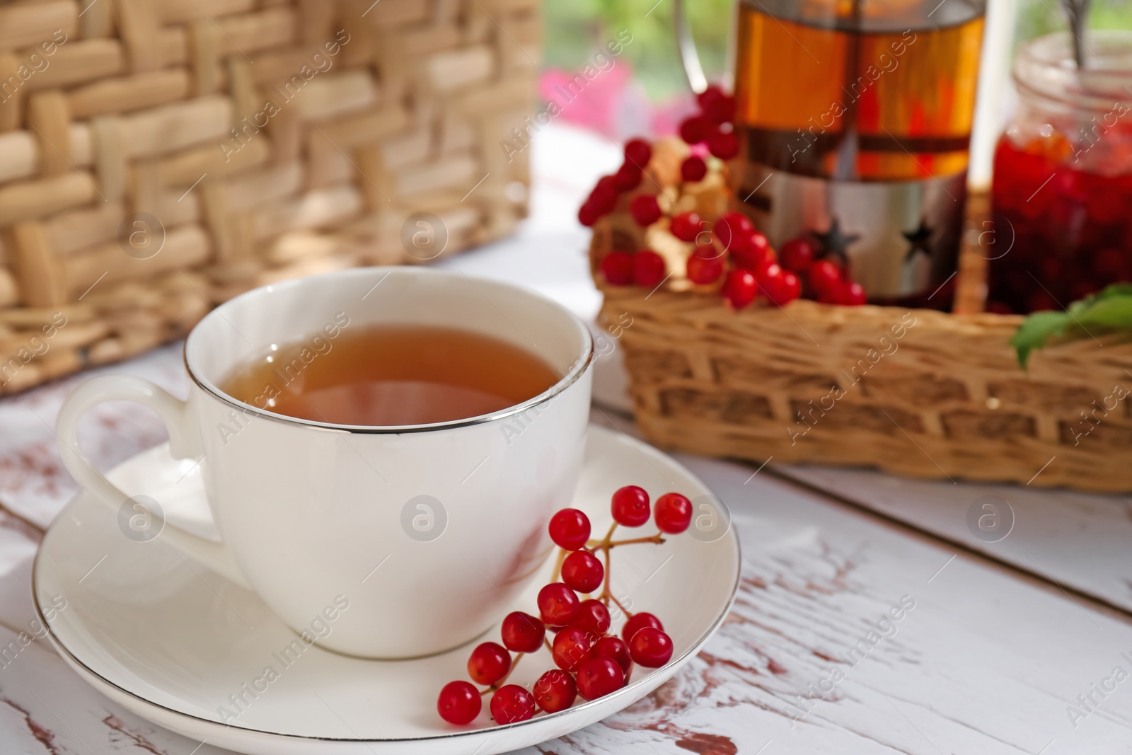 Photo of Cup of hot drink and viburnum berries on white wooden table indoors, closeup