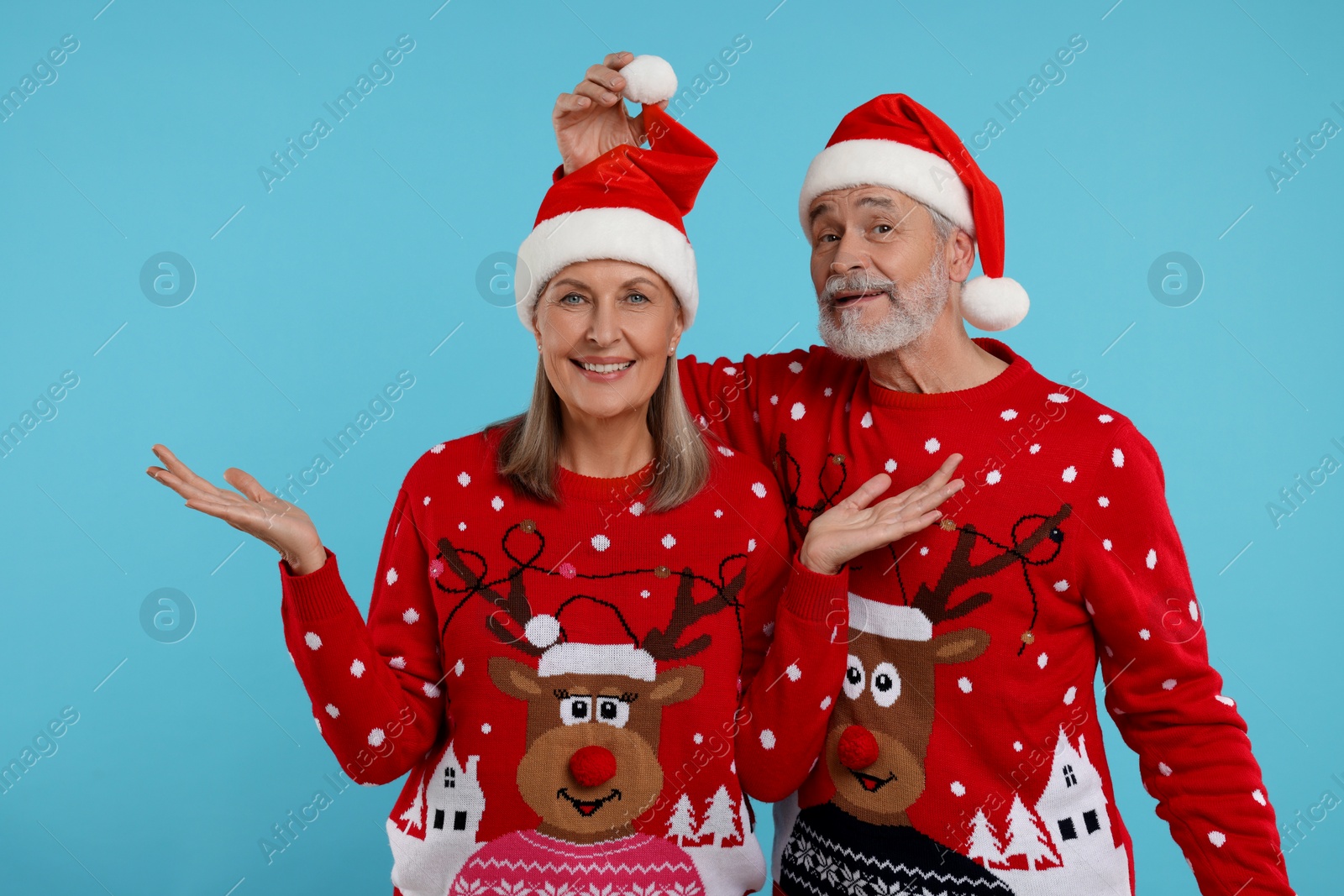 Photo of Happy senior couple in Christmas sweaters and Santa hats on light blue background