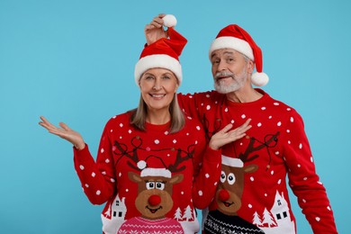 Photo of Happy senior couple in Christmas sweaters and Santa hats on light blue background