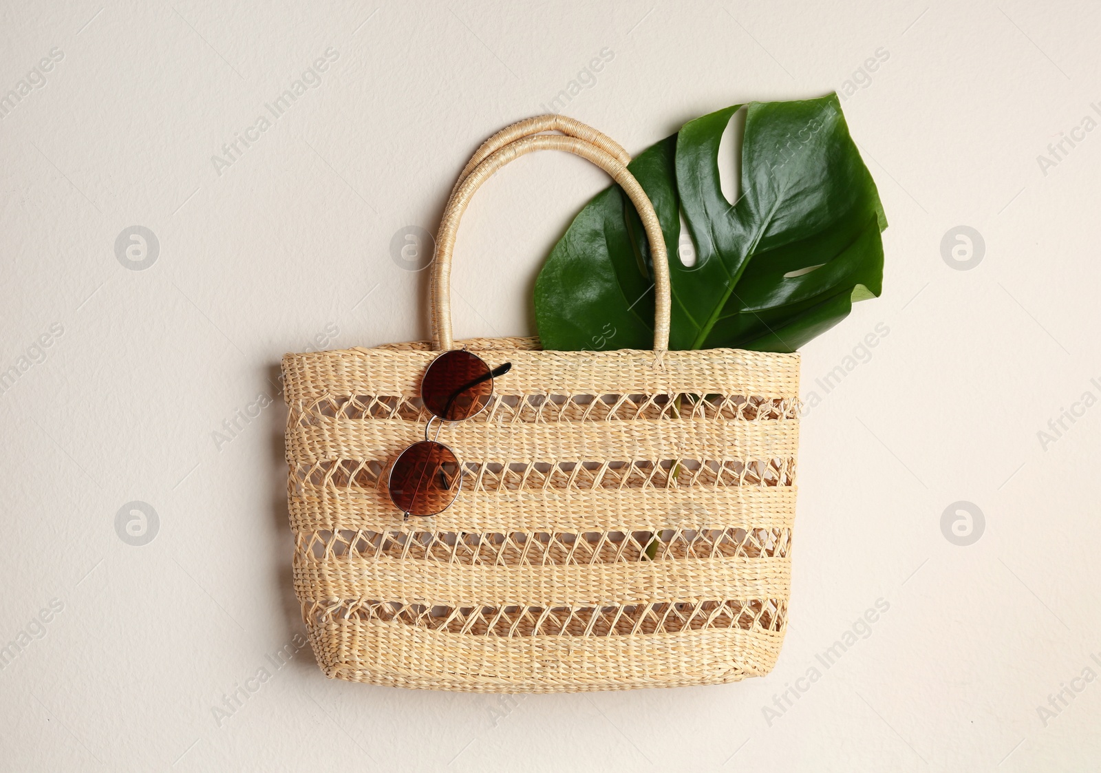 Photo of Elegant woman's straw bag with tropical leaf and sunglasses on beige background, top view
