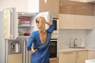 Photo of Young woman standing near open refrigerator in kitchen
