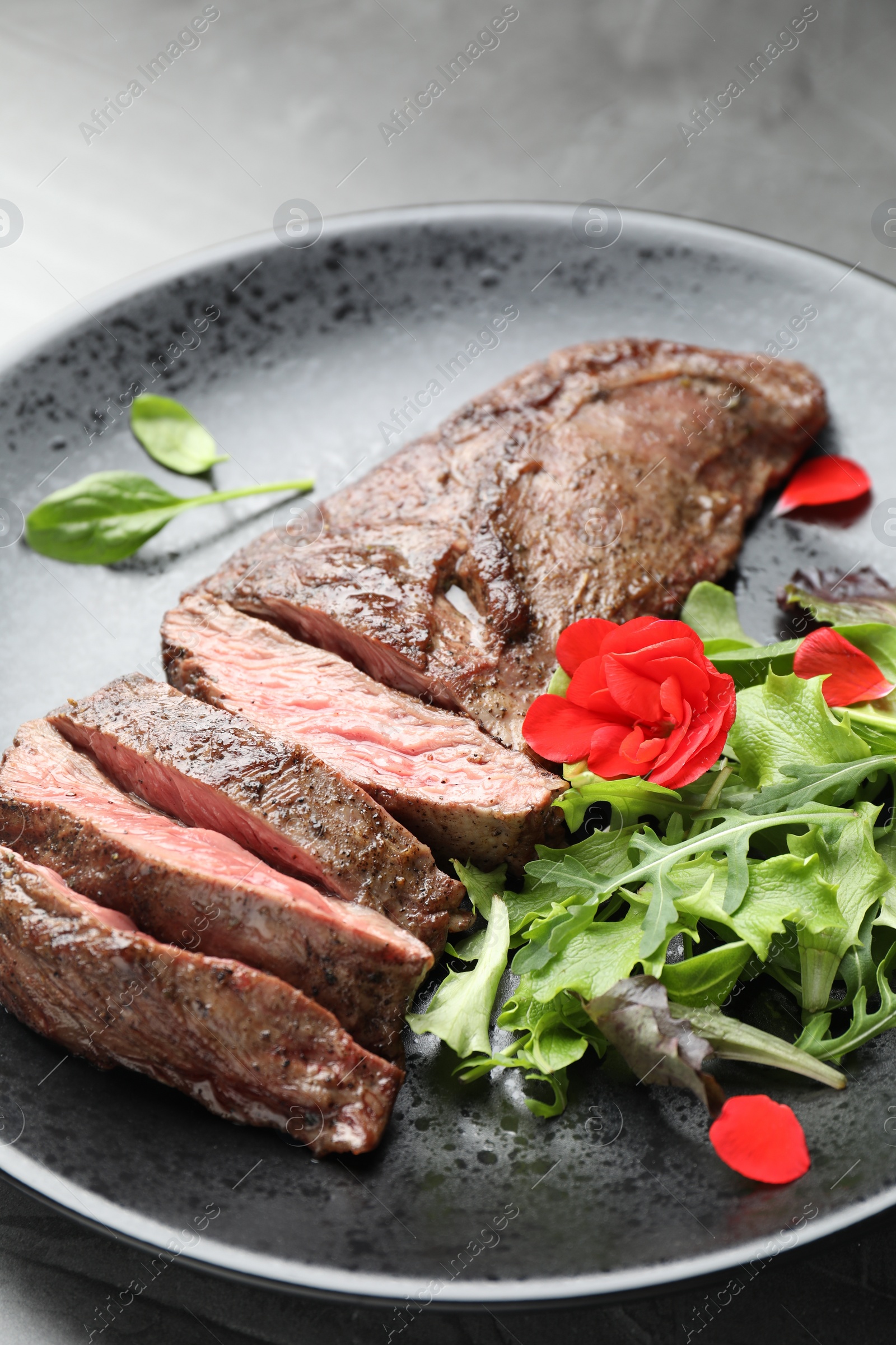 Photo of Pieces of delicious grilled beef meat and greens on table, closeup