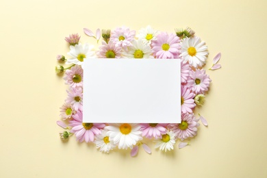 Beautiful chamomile flowers and paper card on color background, flat lay with space for text