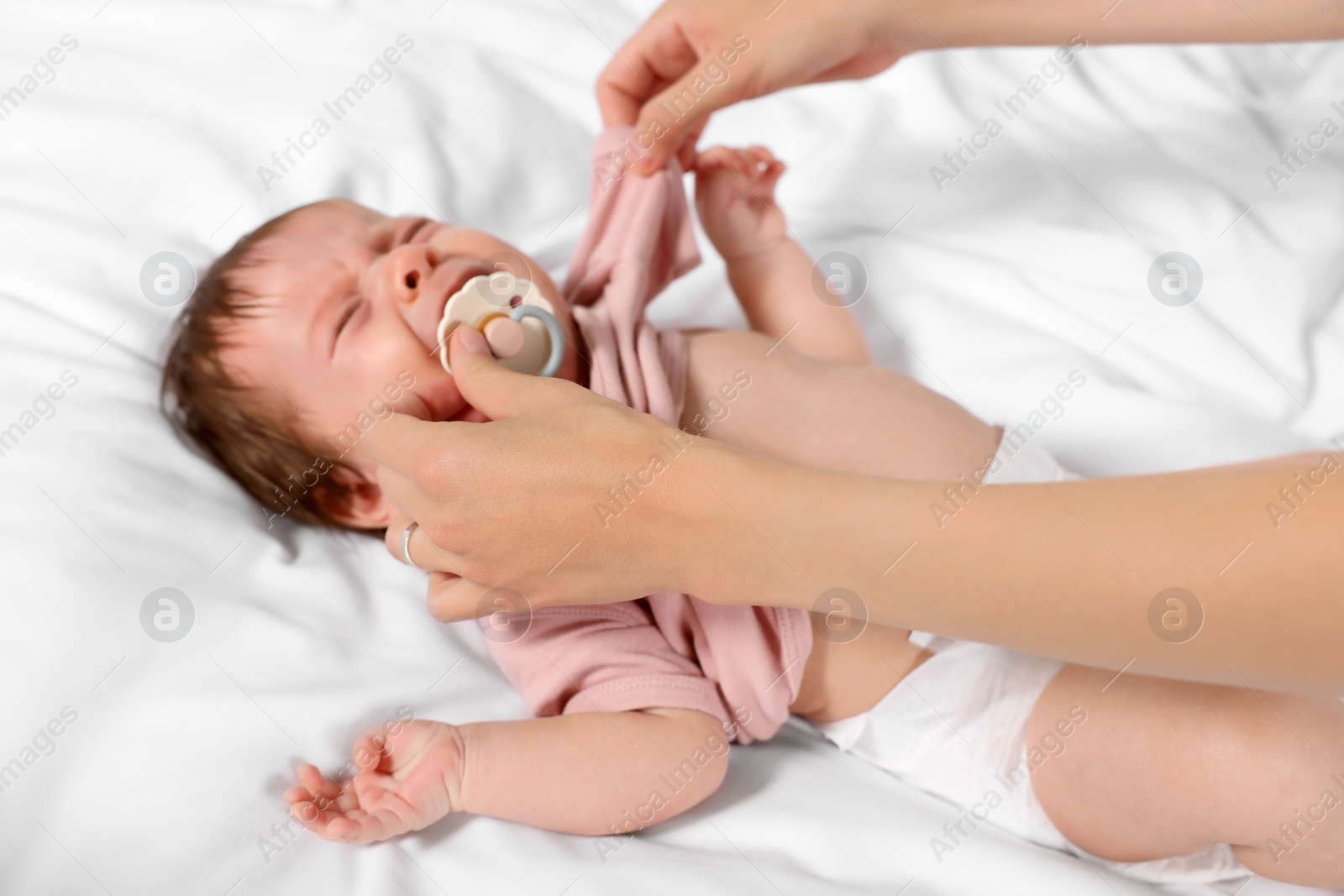 Photo of Mother putting clothes on crying daughter on bed, closeup