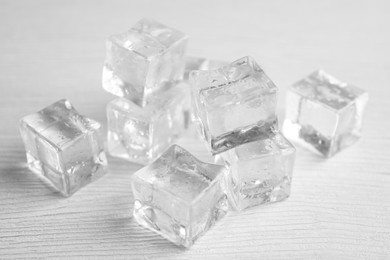 Photo of Ice cubes with water drops on white wooden table, closeup