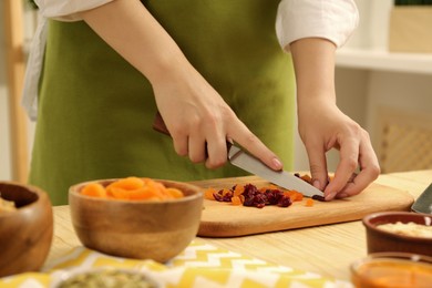 Making granola. Woman cutting dried apricots and cherries at table in kitchen, closeup