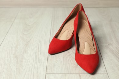 Photo of Orthopedic insoles in high heel shoes on floor, closeup. Space for text