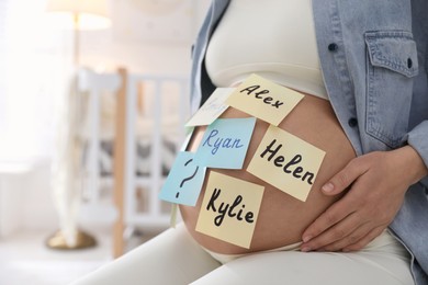 Photo of Pregnant woman with different baby names on belly at home, closeup. Space for text