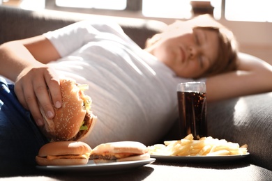 Overweight boy sleeping on sofa surrounded by fast food