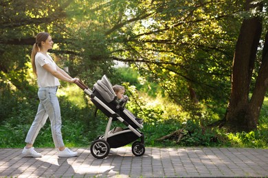 Photo of Happy nanny with baby in stroller walking in park, space for text