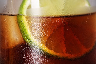 Glass of refreshing drink with sliced lime and ice cubes as background, closeup