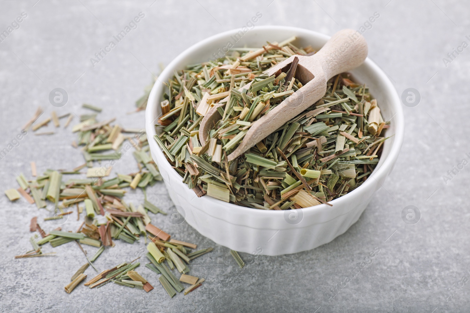 Photo of Bowl with aromatic dried lemongrass and scoop on light grey table