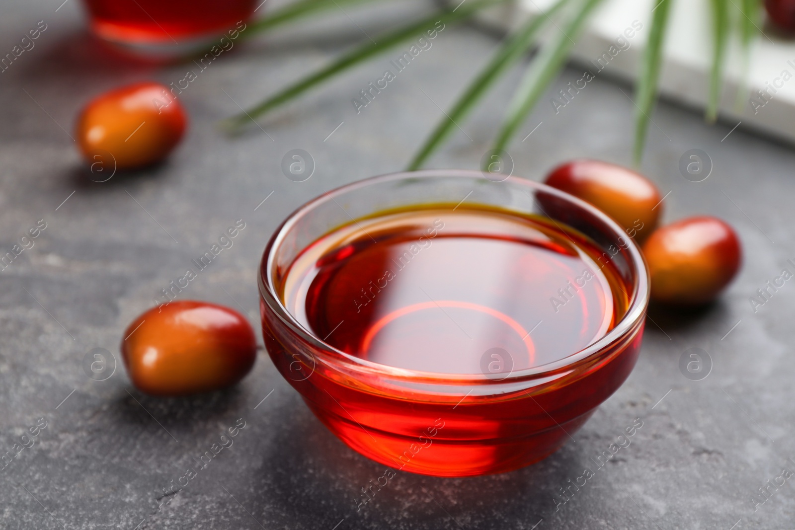 Photo of Palm oil in glass bowl, tropical leaf and fruits on grey table