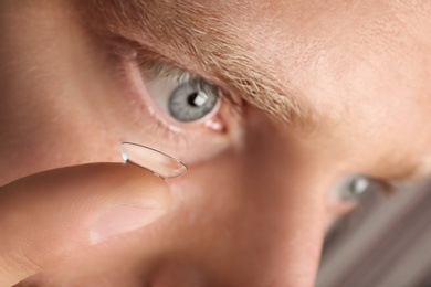 Young man putting contact lens into his eye, closeup