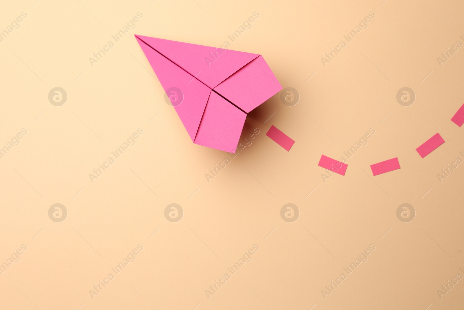Photo of Handmade pink paper plane with dotted lines on beige background, top view. Space for text