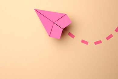 Photo of Handmade pink paper plane with dotted lines on beige background, top view. Space for text