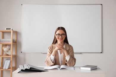 Photo of Happy young teacher sitting at table in classroom