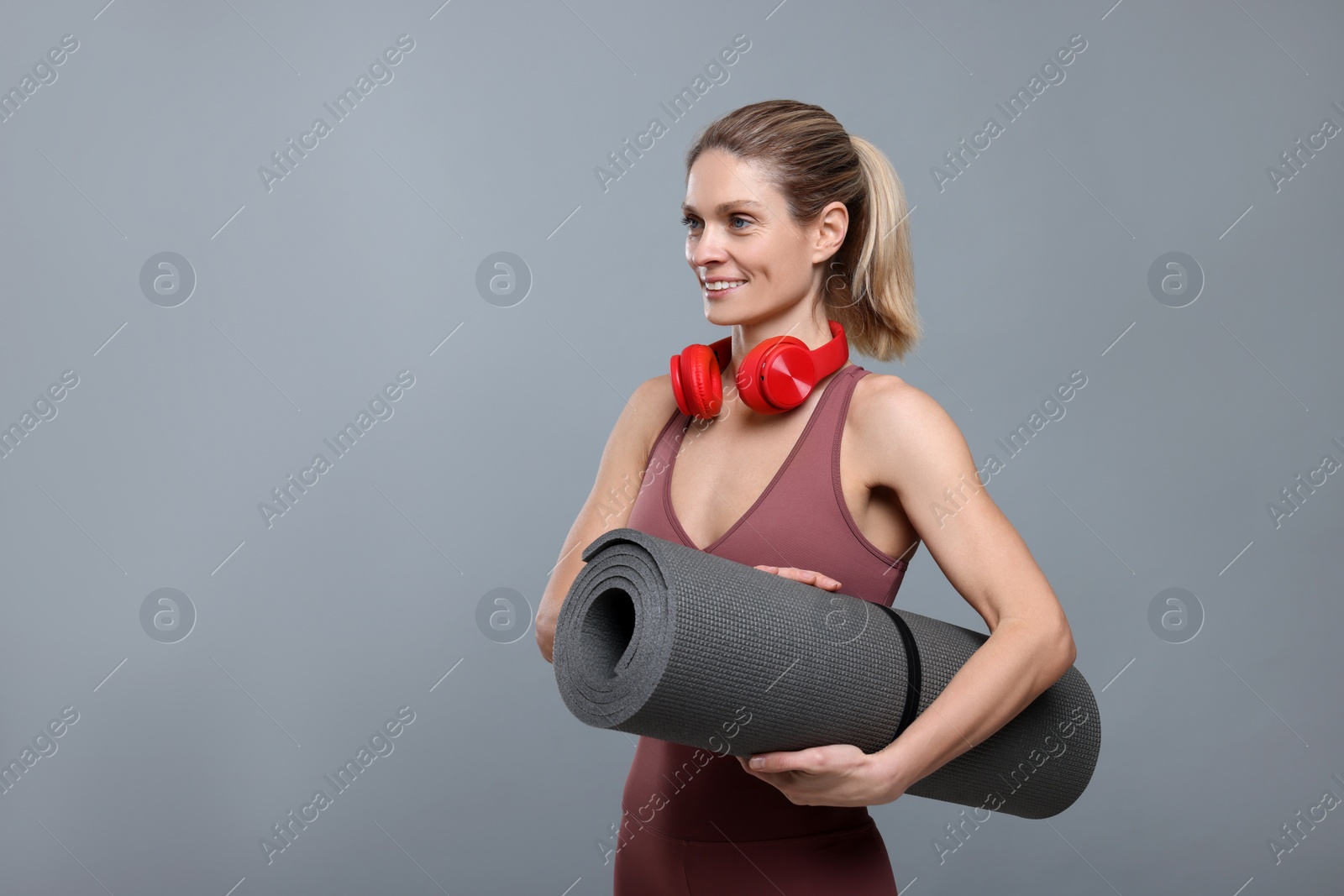 Photo of Sportswoman with headphones and fitness mat on grey background, space for text