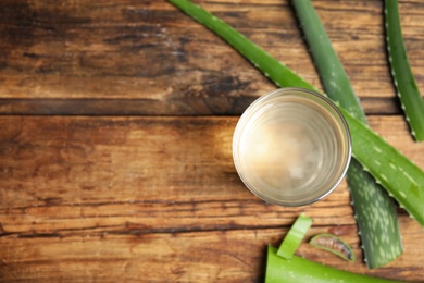 Photo of Fresh aloe drink in glass and leaves on wooden table, flat lay. Space for text