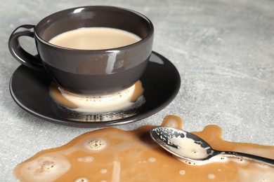 Photo of Cup, saucer and spoon near spilled coffee on grey table, closeup