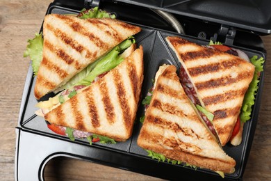 Photo of Modern grill maker with sandwiches on wooden table, top view