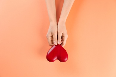 Woman holding decorative heart on color background, top view