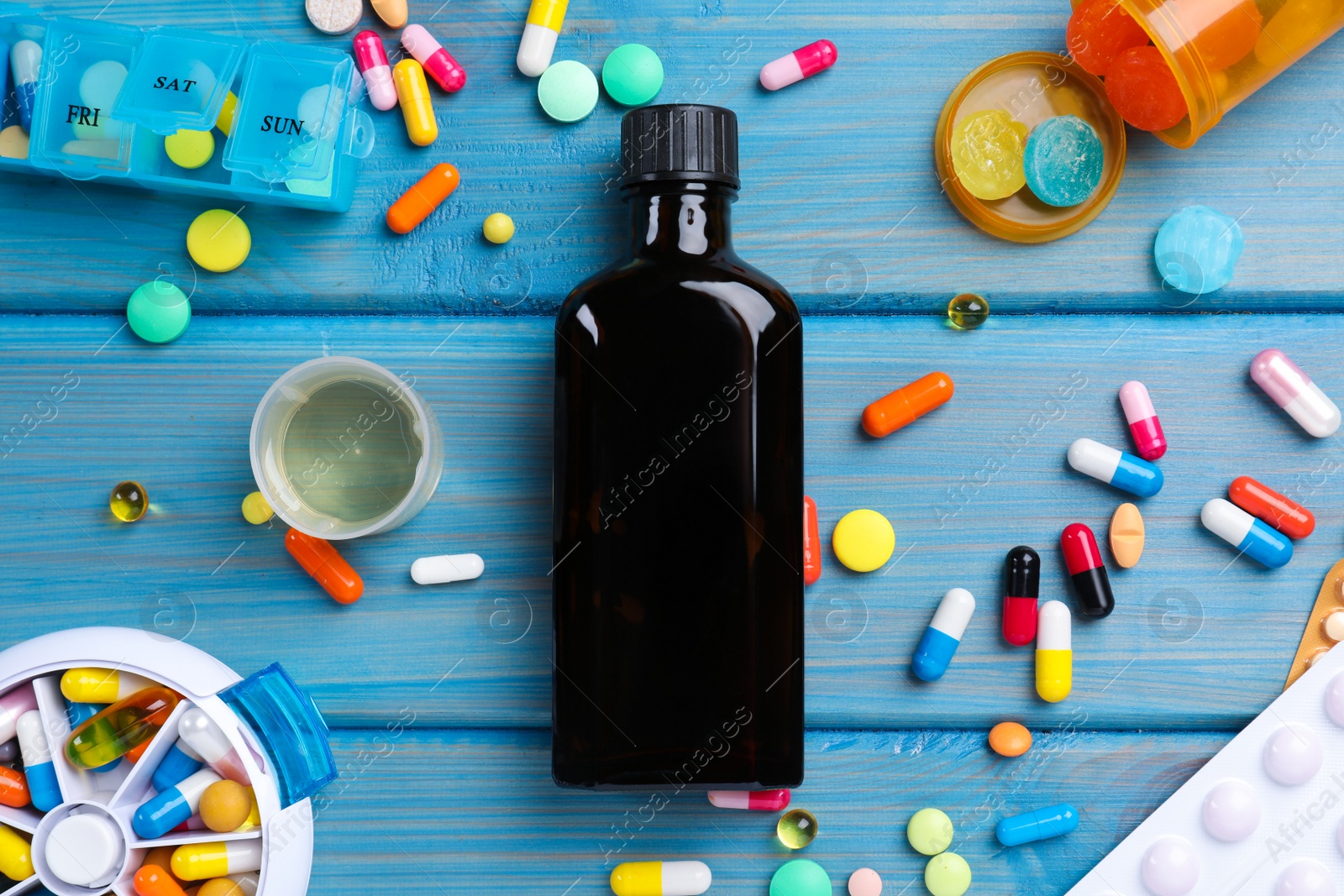 Photo of Flat lay composition with bottle of syrup, measuring cup and pills on light blue wooden table. Cold medicine