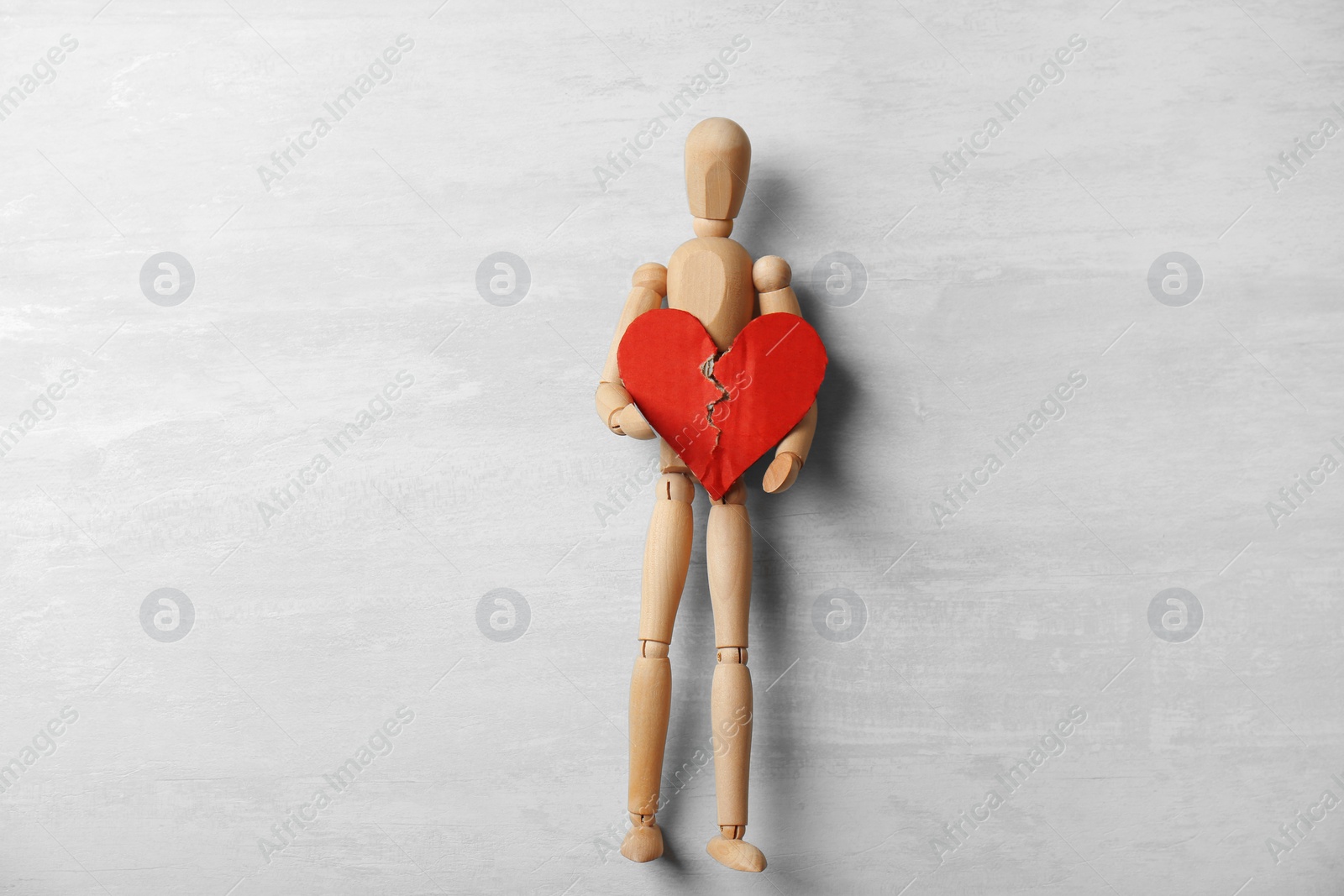 Photo of Wooden puppet with torn cardboard heart on gray background, top view. Relationship problems