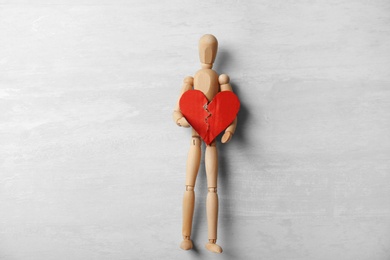 Photo of Wooden puppet with torn cardboard heart on gray background, top view. Relationship problems