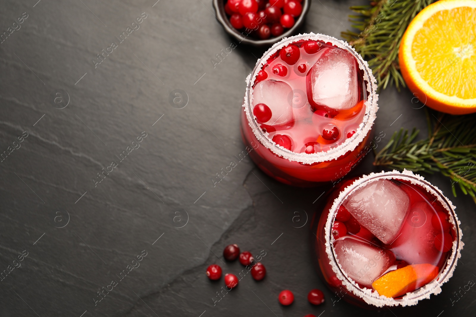 Photo of Tasty cranberry cocktail with ice cubes in glasses on dark gray textured table, flat lay. Space for text