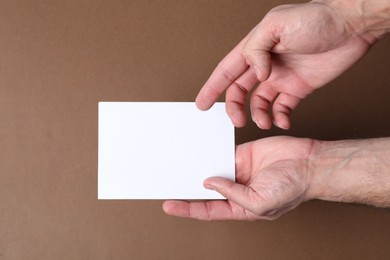 Man holding flyer on brown background, top view. Mockup for design