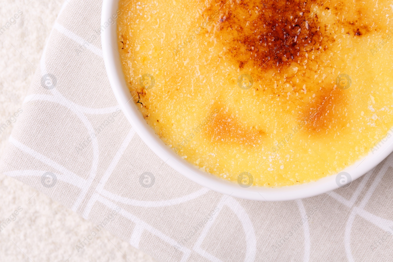 Photo of Delicious creme brulee in bowl on light textured table, top view. Space for text