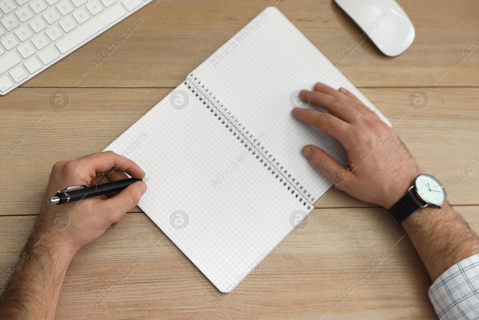 Photo of Left-handed man writing in notebook at wooden table, top view