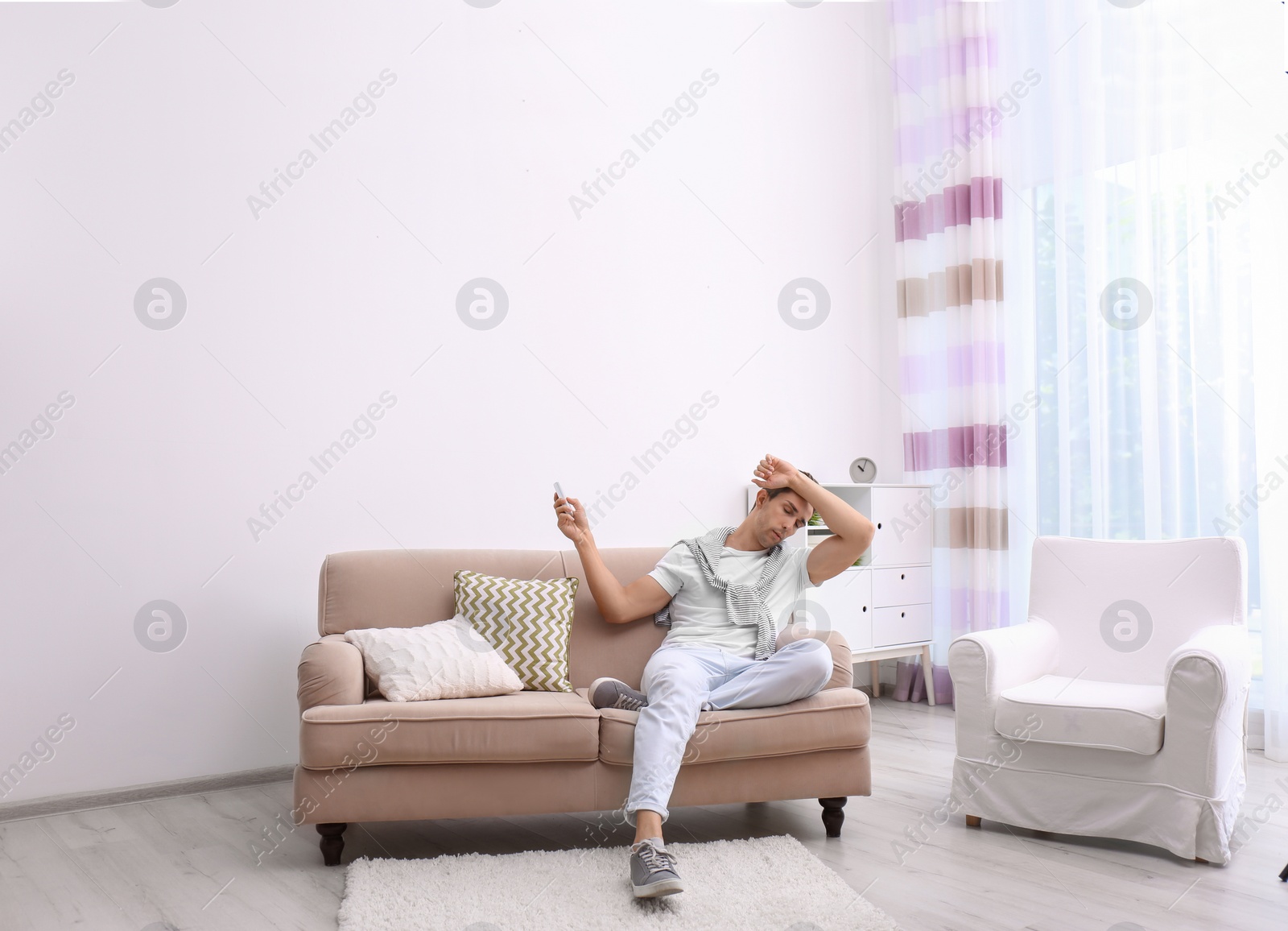 Photo of Young man operating air conditioner with remote control at home