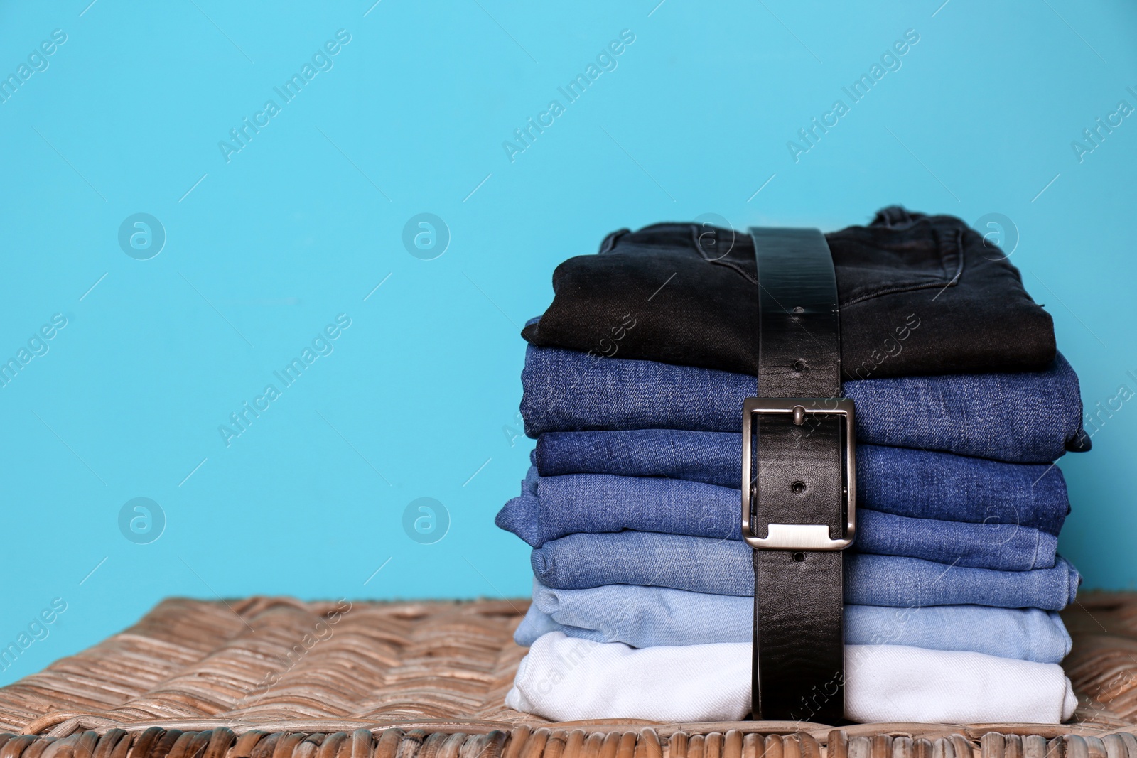 Photo of Stack of different jeans on basket against color wall with space for text