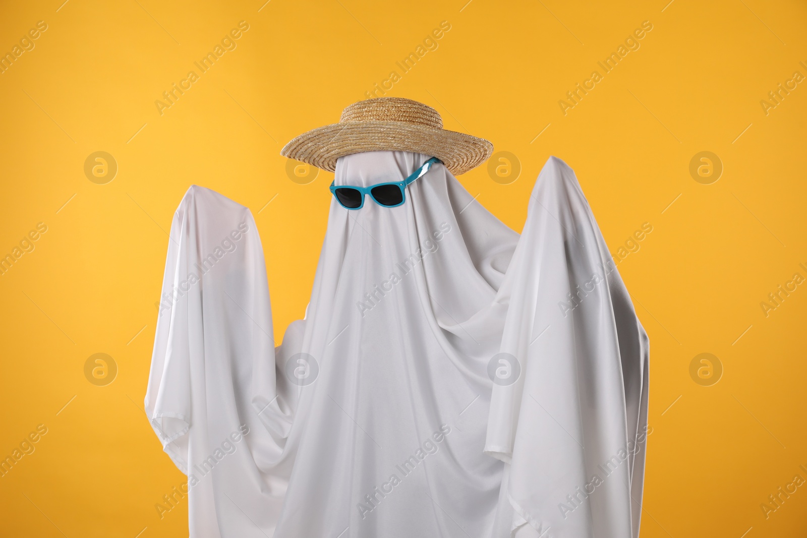 Photo of Person in ghost costume, sunglasses and straw hat on yellow background