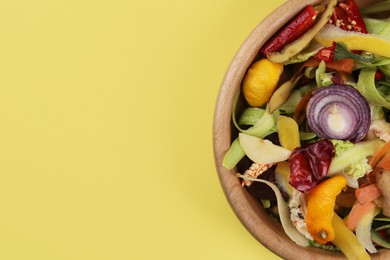 Peels of fresh vegetables in bowl on yellow background, top view. Space for text