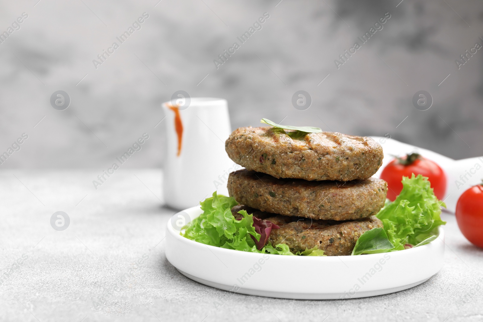 Photo of Delicious grilled vegan cutlets with lettuce on light grey table, closeup. Space for text