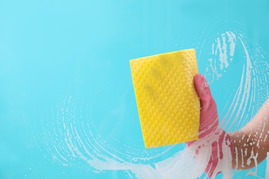 Photo of Woman cleaning glass with rag against color background