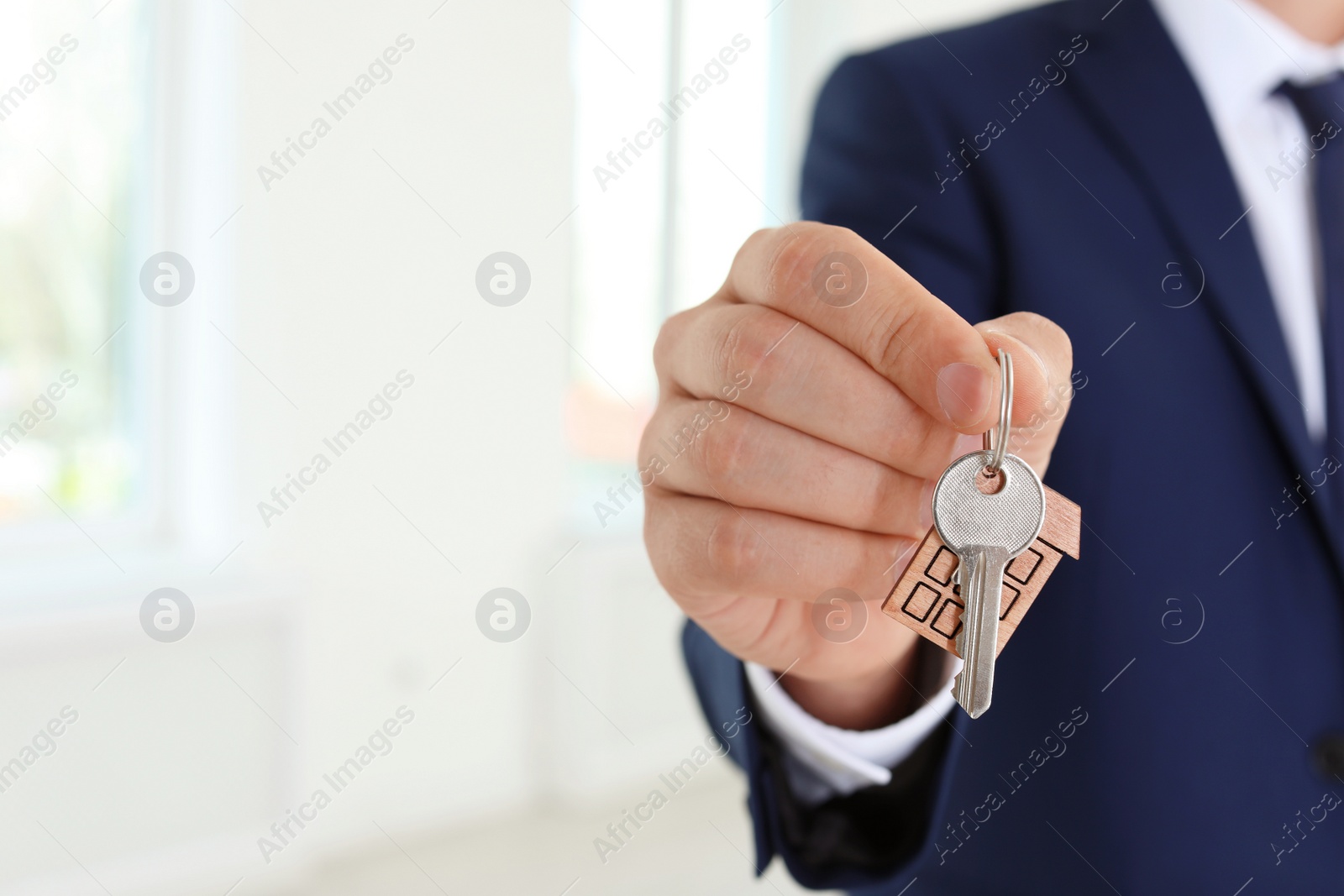 Photo of Real estate agent holding key on blurred background, closeup