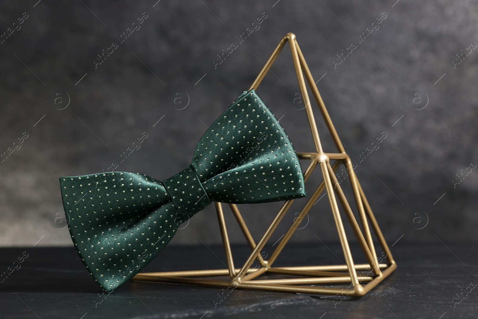 Photo of Stylish presentation of green bow tie on black table against gray background