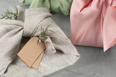 Photo of Furoshiki technique. Gifts packed in fabric on grey table, closeup