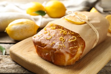 Photo of Wrapped tasty lemon cake with glaze on wooden table, closeup