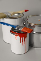 Cans of orange paint and brushes on grey background