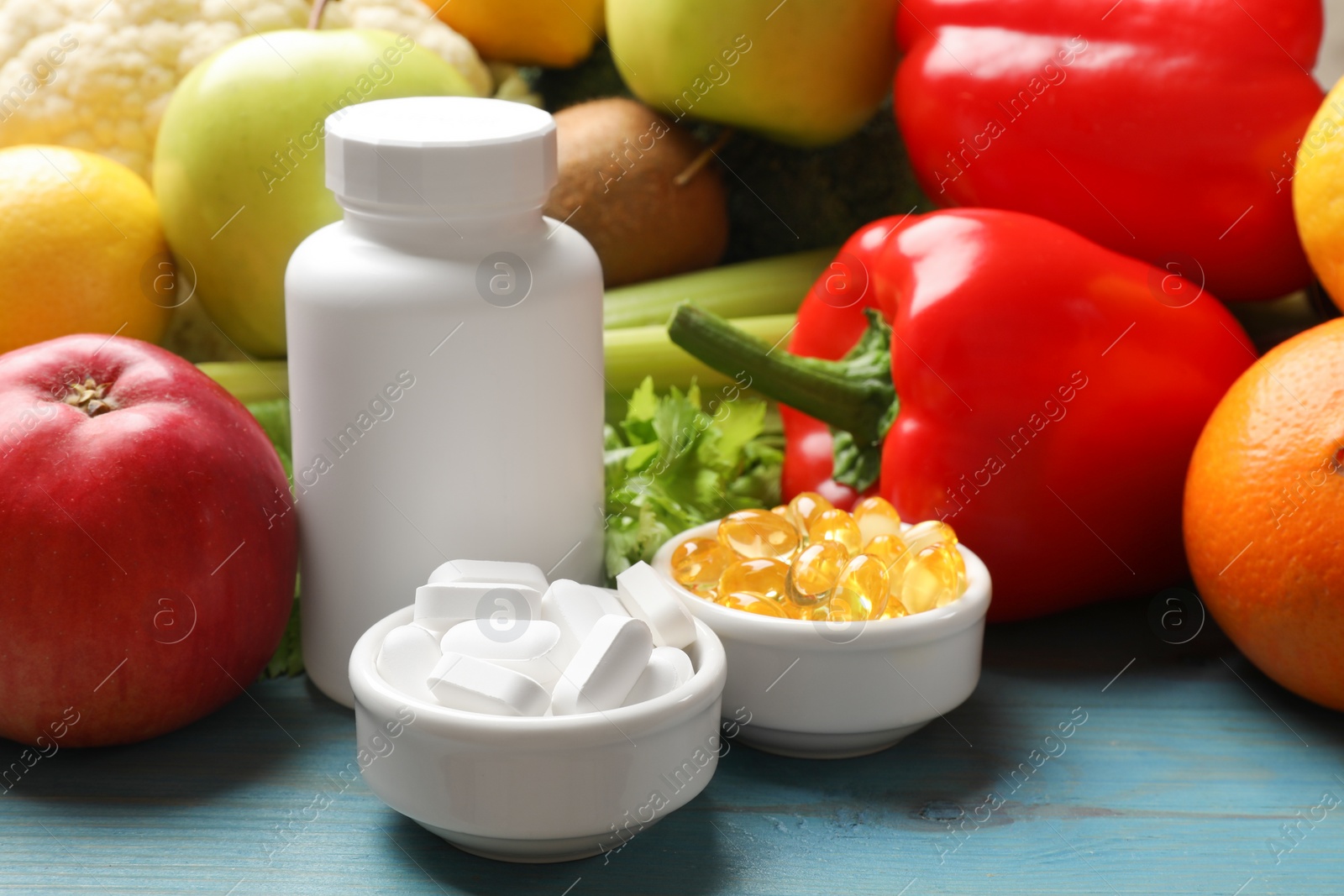 Photo of Dietary supplements. Blank white bottle and bowls with different pills near food products on light blue wooden table