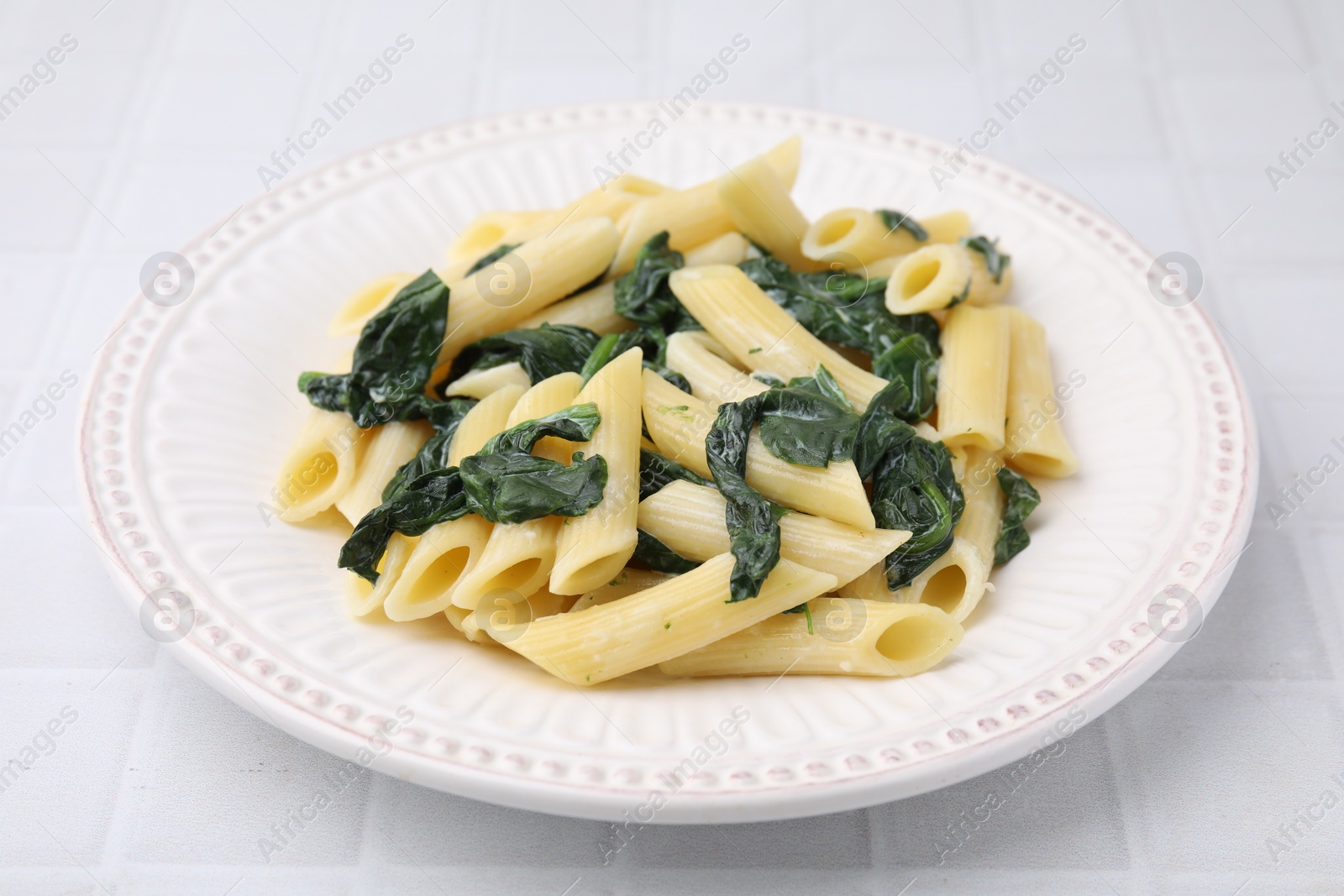 Photo of Tasty pasta with spinach and sauce on white tiled table