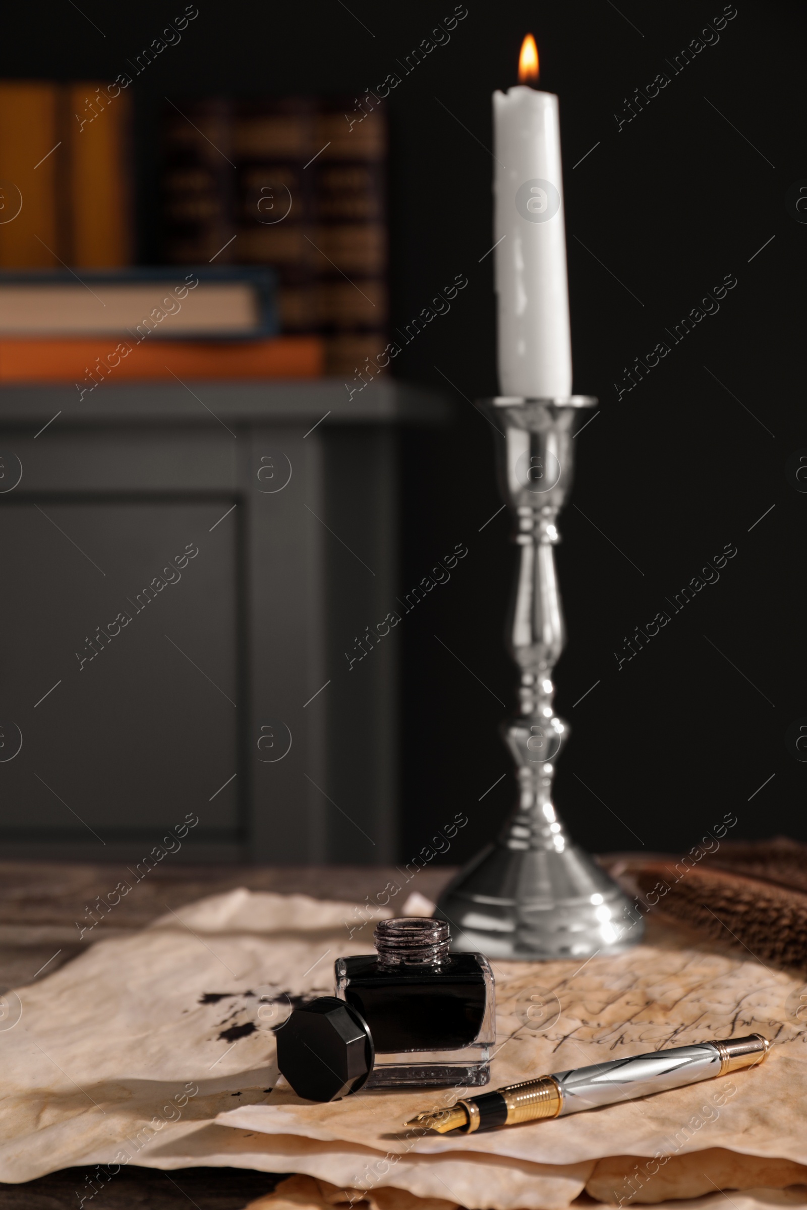 Photo of Inkwell, fountain pen, candlestick and vintage parchment with ink stains on wooden table indoors. Space for text