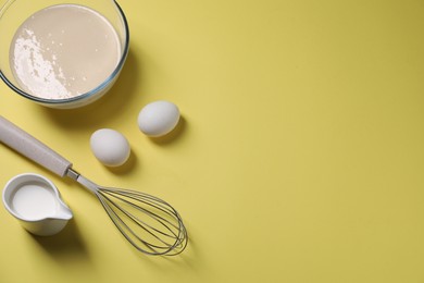 Photo of Metal whisk, dough in bowl, eggs and milk on pale yellow background, flat lay. Space for text