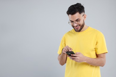 Happy young man using smartphone on grey background, space for text